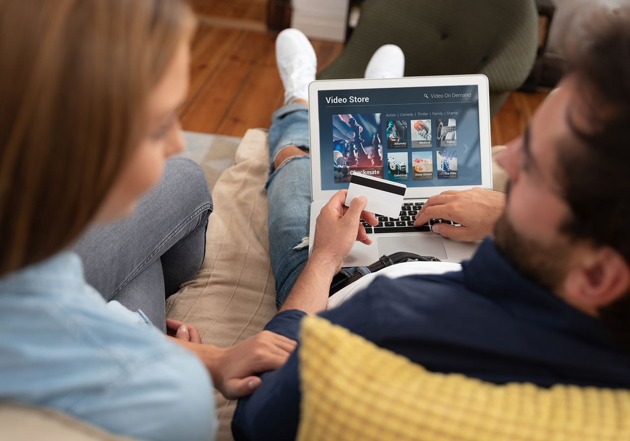 A man and woman sit together on a couch, focused on a laptop in front of them.