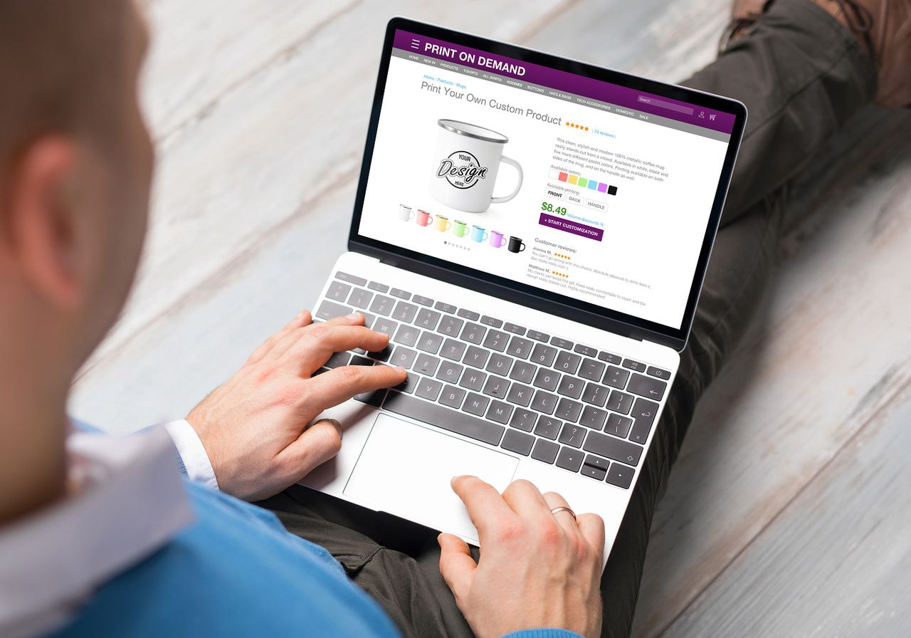 A man sits on a wooden floor, focused on his laptop, surrounded by a cozy indoor environment.