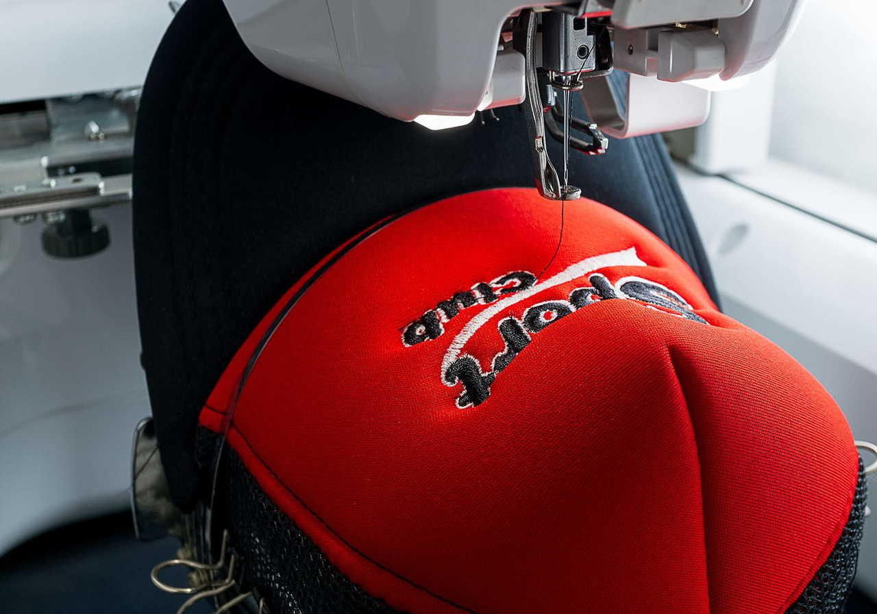 Close-up of a sewing machine embroidering a logo on a red cap.