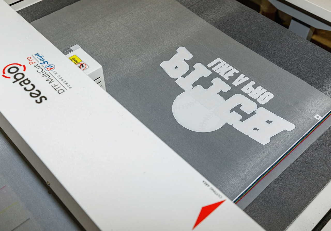 A layer with a baseball-themed design (“PITCH LIKE A PRO” text) is being prepared to be printed on a t-shirt using DTF printing.