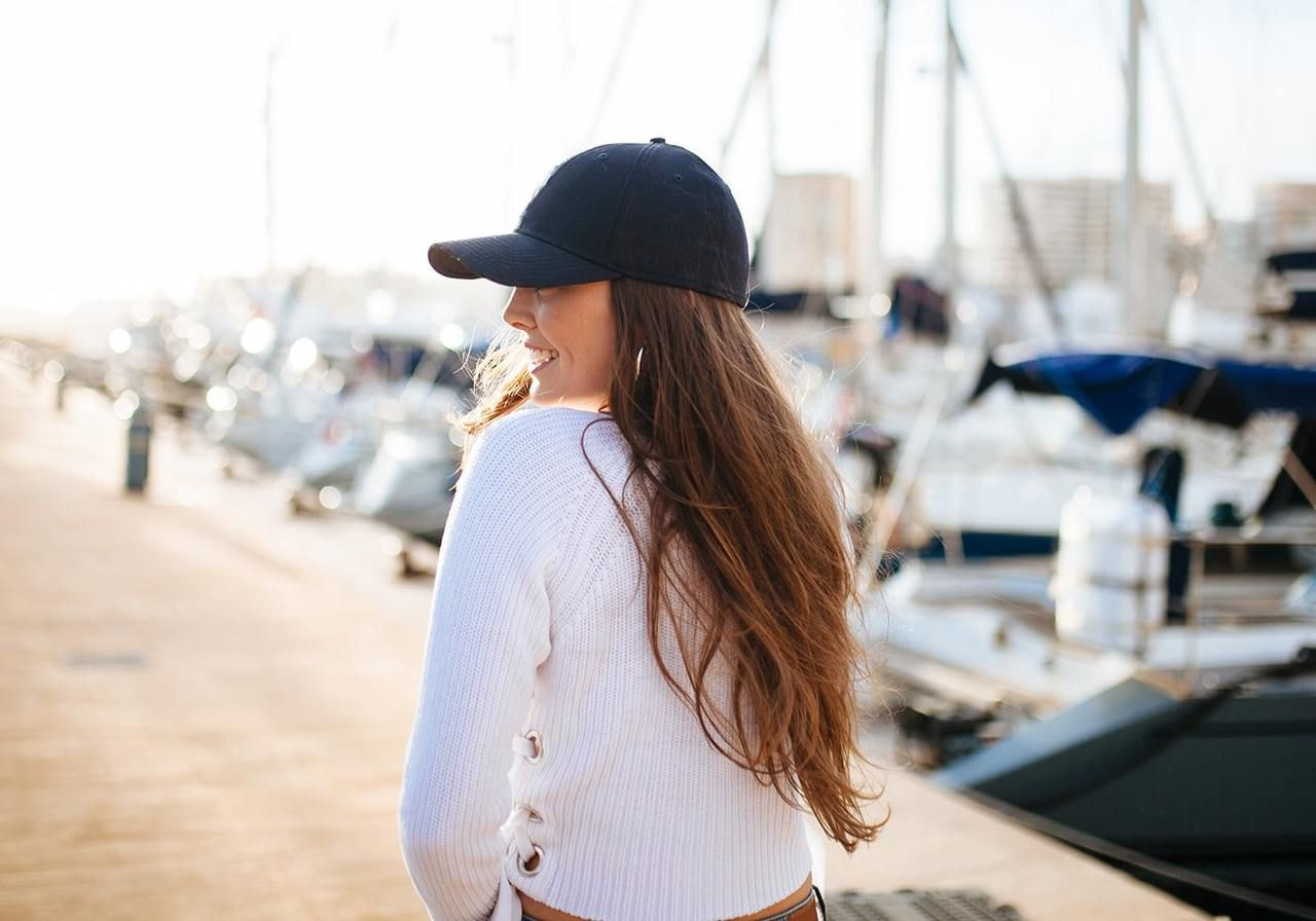 A backshot of a woman looking to the side, wearing a black 5-panel hat.