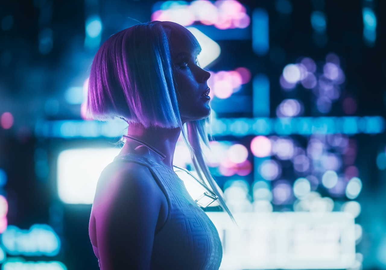 A woman with a futuristic bob haircut is illuminated by neon lights, creating a vibrant, cyberpunk atmosphere in the cityscape
