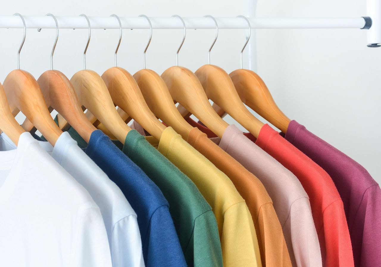Row of colorful t-shirts on wooden hangers arranged in rainbow order.