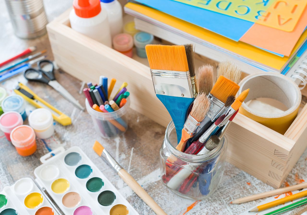 A table displaying an assortment of children's art supplies, including paints, brushes, markers, and paper.