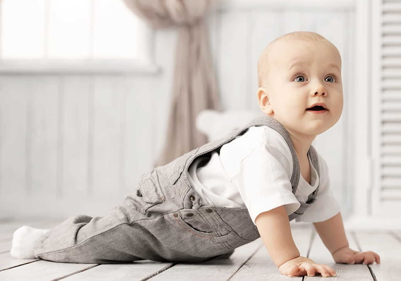 A small child in a white t-shirt and gray denim overalls is looking up and sideways.