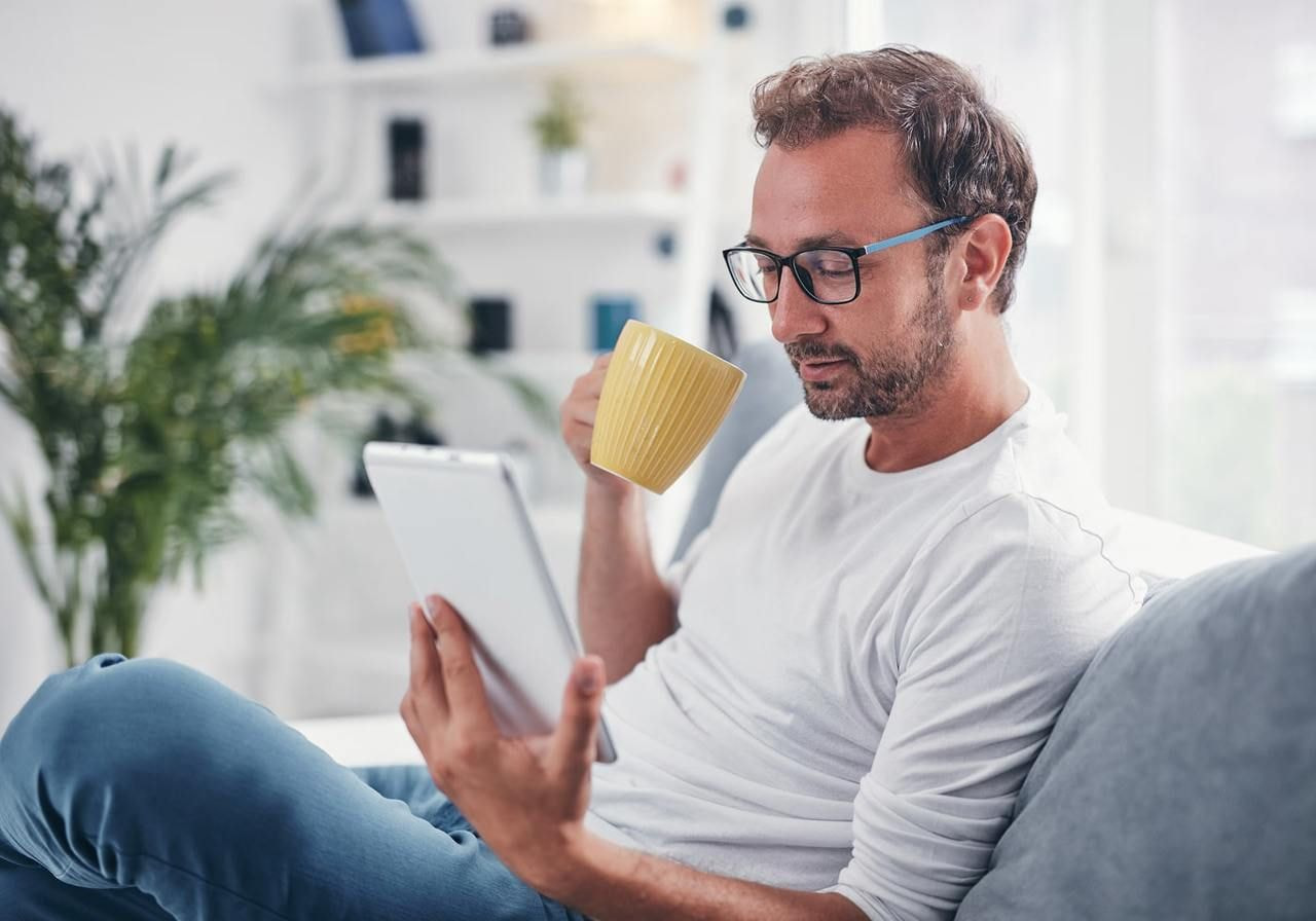 A man is drinking from a mug while reading news on Mexico tariffs from a tablet.