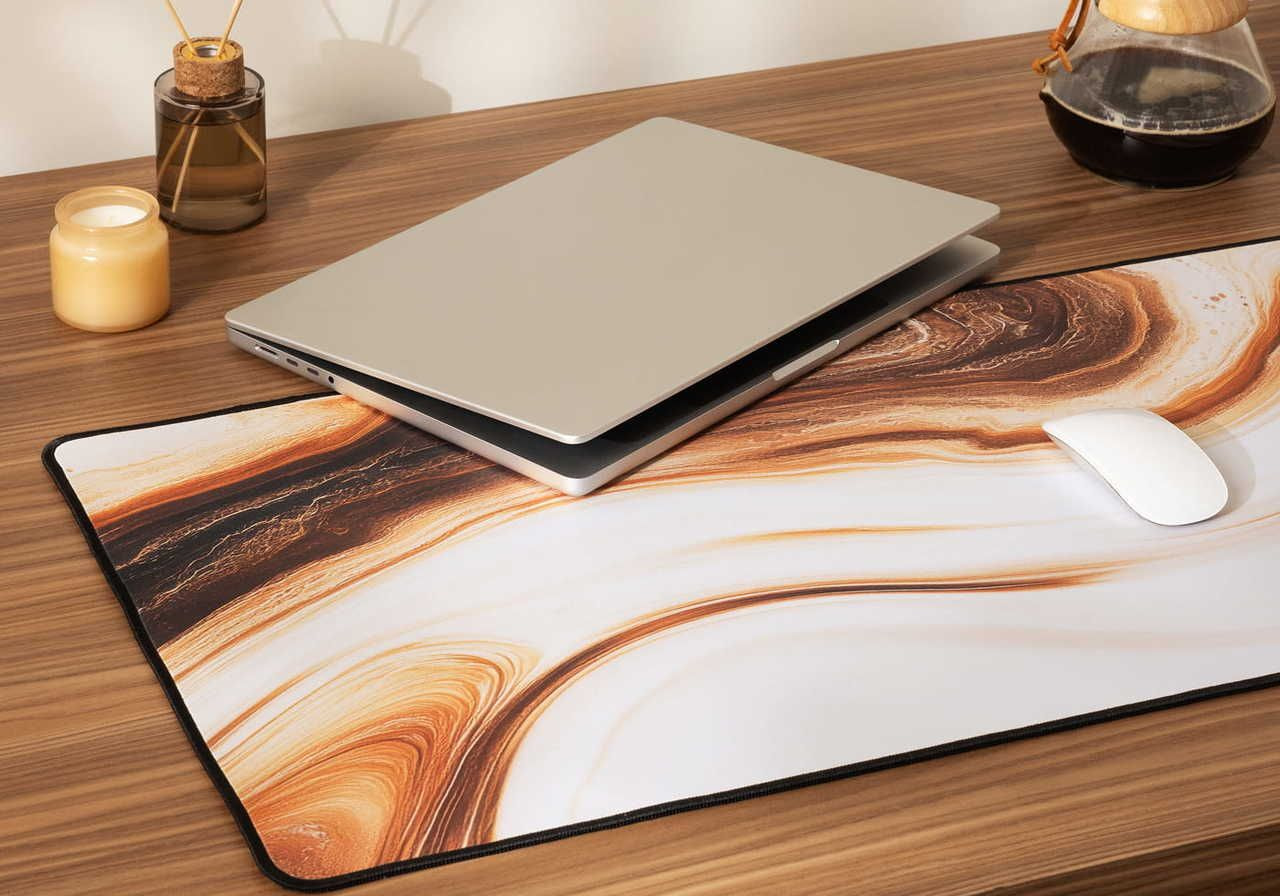 A laptop and a mouse are placed on a decorative mouse pad with a marble-like design, resting on a wooden surface.