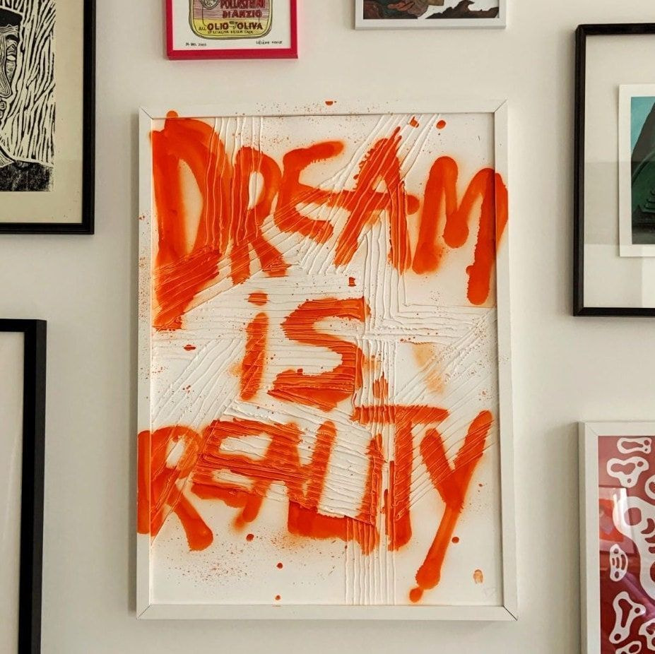 A framed poster displaying the phrase "Dream is Reality" in bold letters against a simple background.