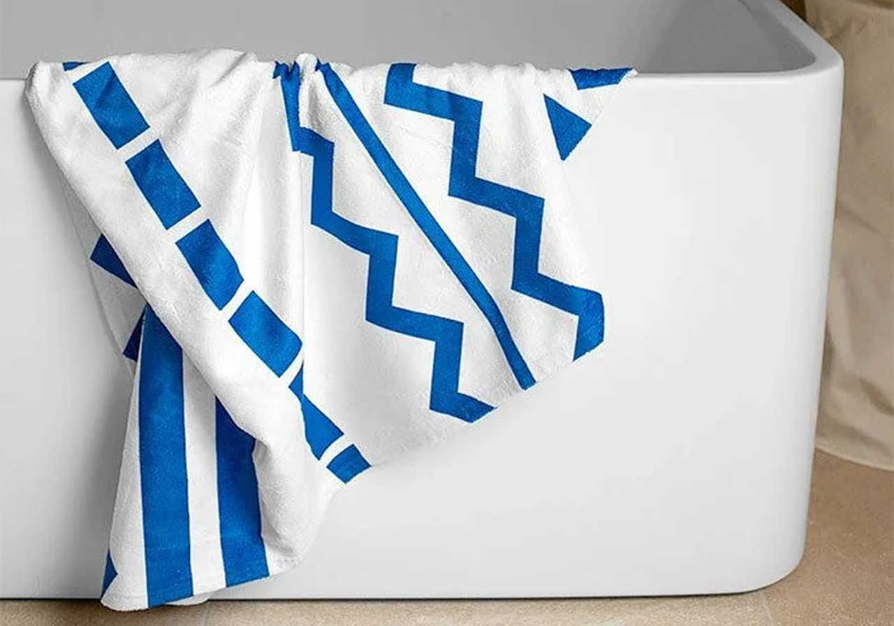 A white towel with blue zigzag and stripe patterns drapes over a modern, white bathtub.
