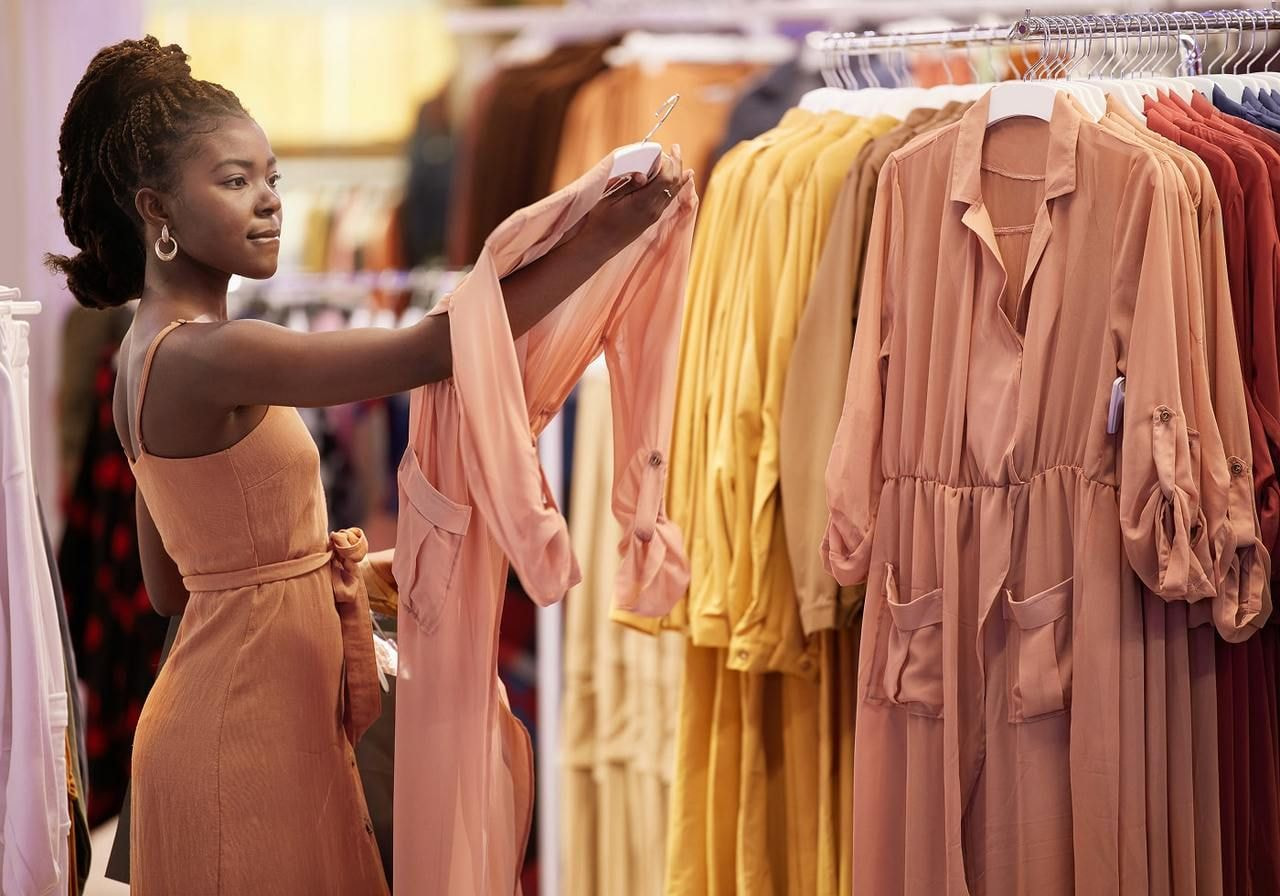 A woman browsing through clothing racks in a retail store, examining various garments.
