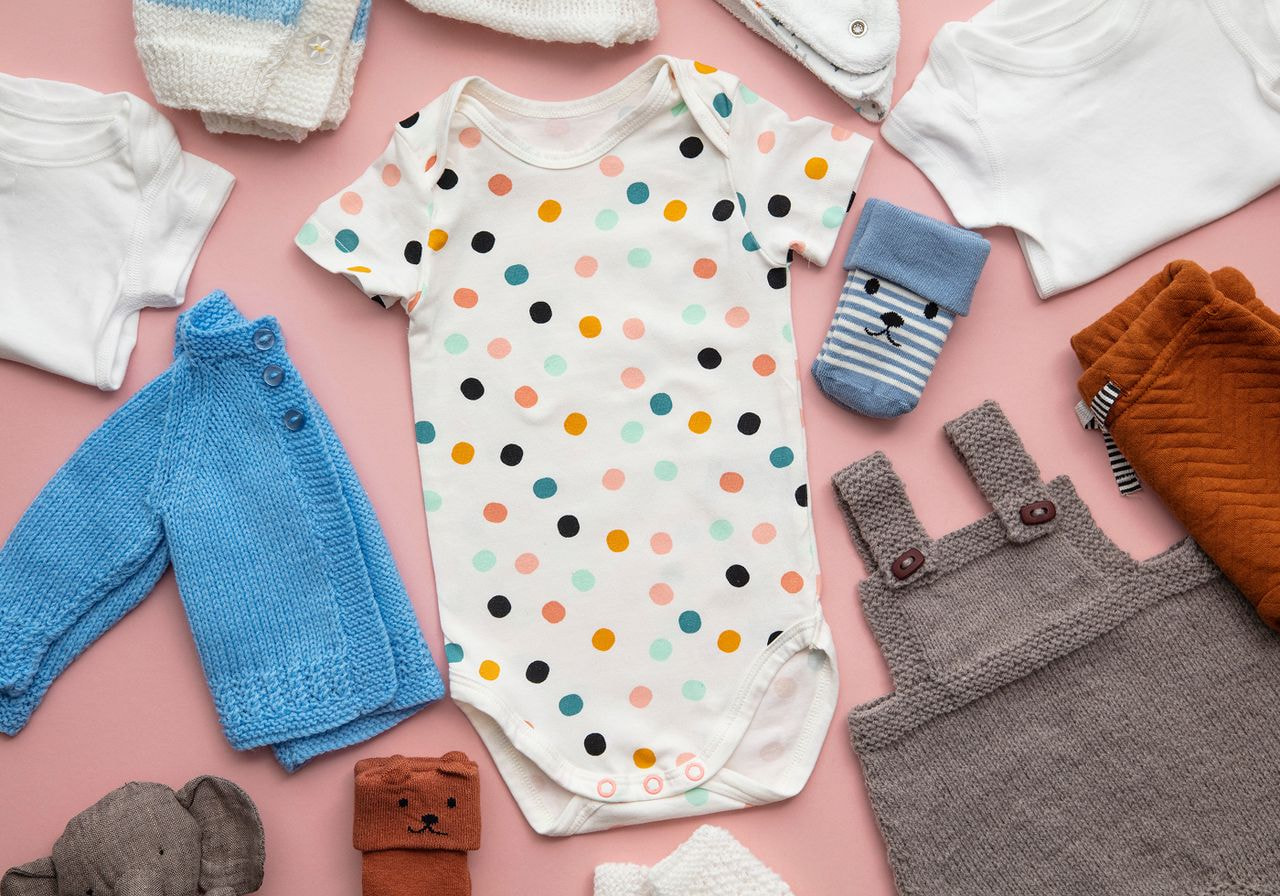 Baby clothes arranged neatly on a soft pink background, showcasing various sizes and styles for infants.