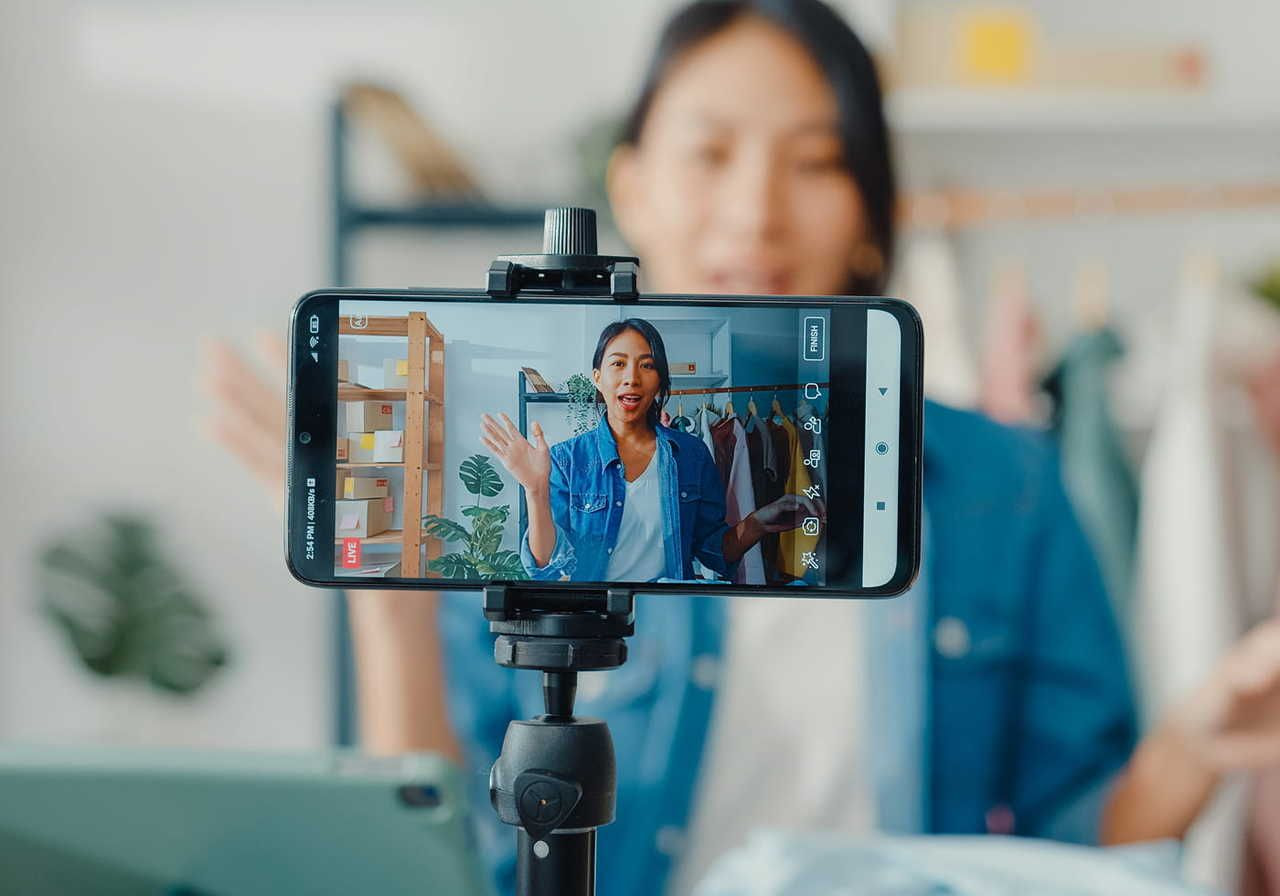 Woman recording a vlog on a smartphone, set on a tripod.