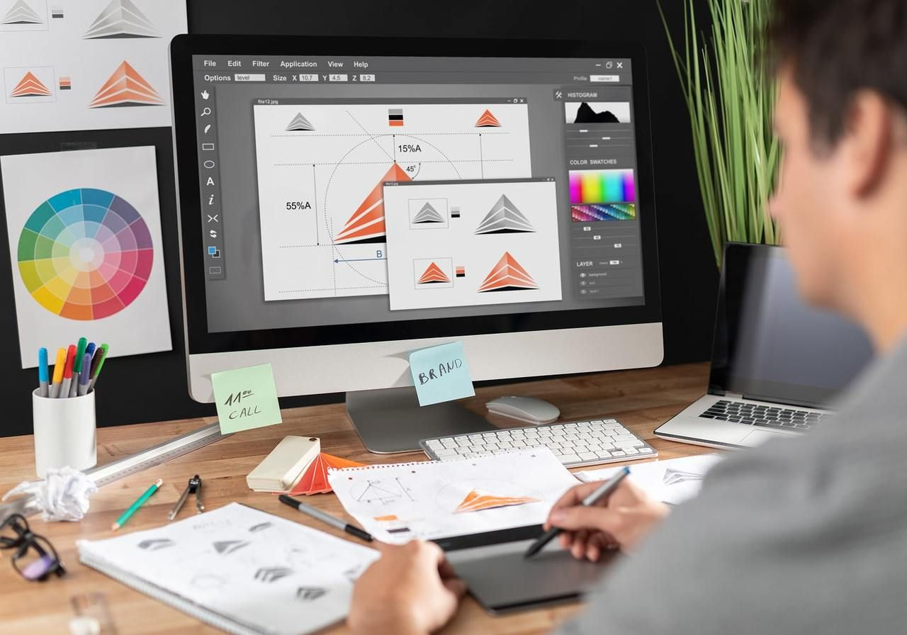 A man is sitting in front of a monitor and designing visual brand identity elements.