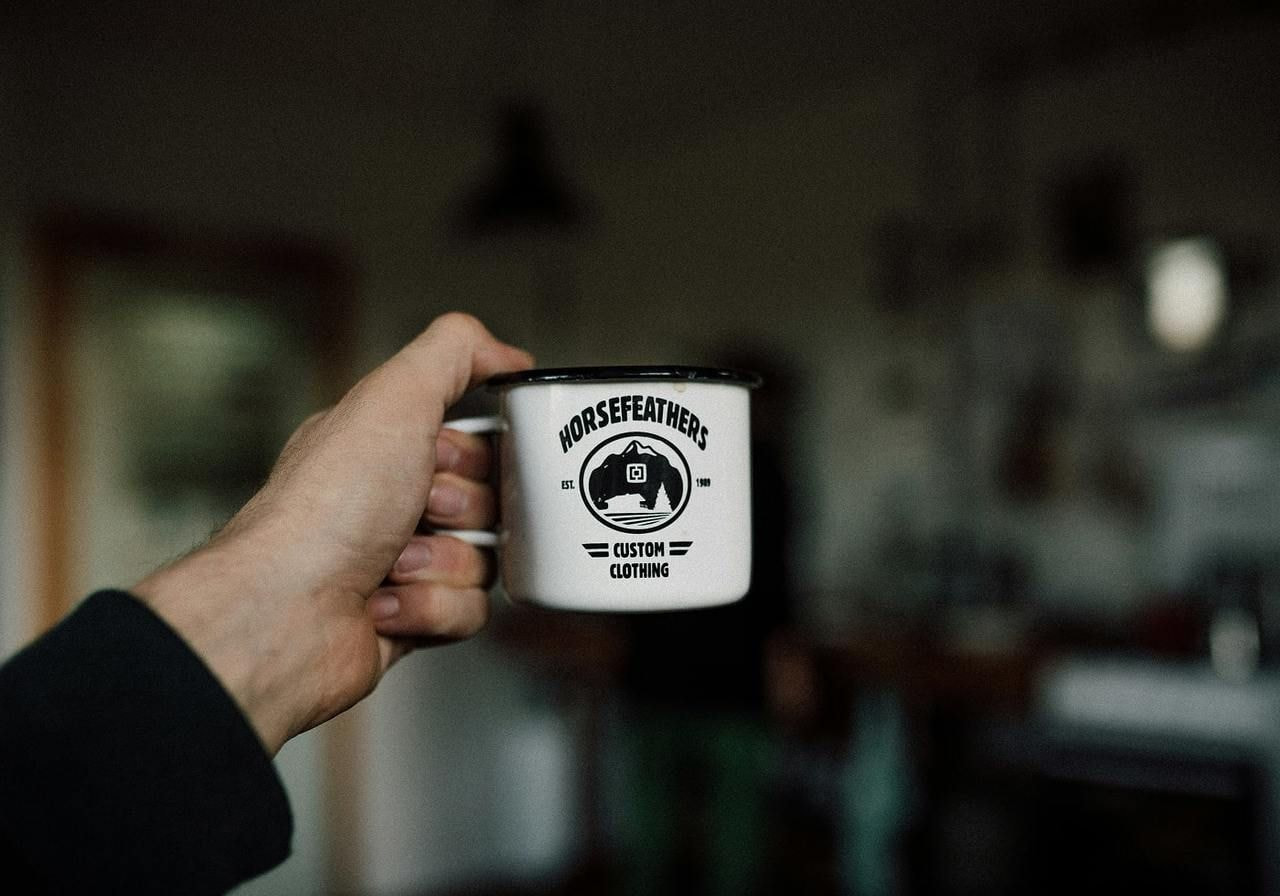 A person is holding a white enamel cup with a print as an example of corporate merch.