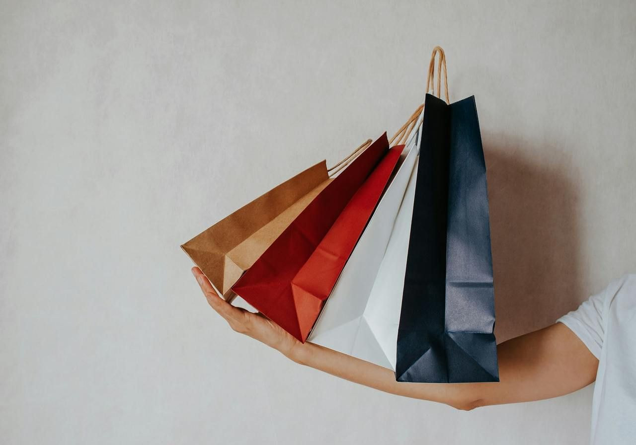Man holding several shopping bags in one hand, smiling while standing in a retail environment.
