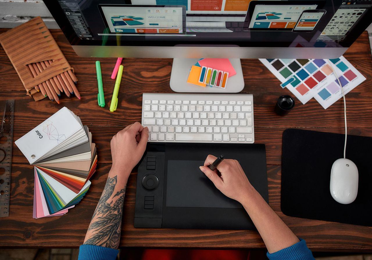 A person using a computer, holding a pen in one hand and a mouse in the other, focused on their work.