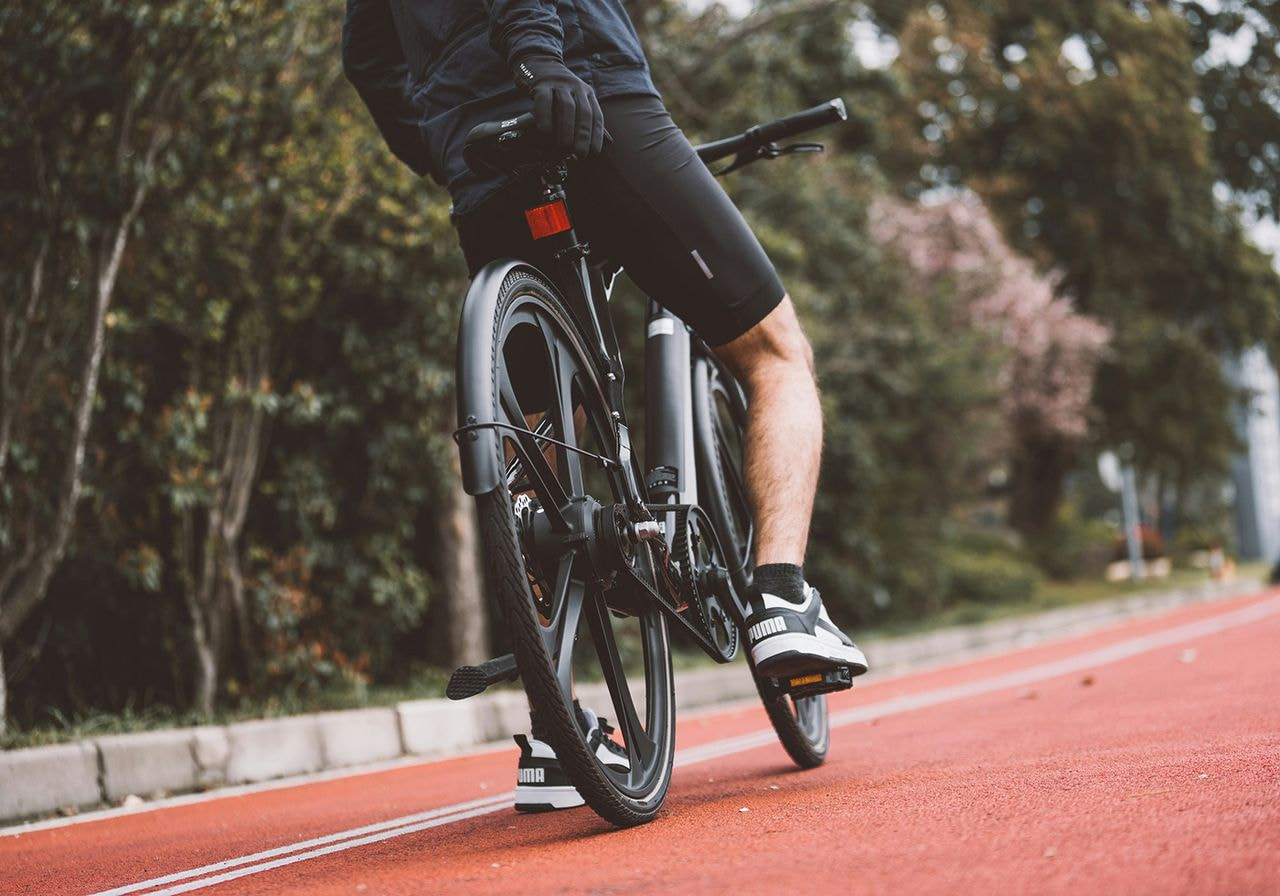 Cyclist on a black bike rides along a red track surrounded by trees. Dressed in black shorts and shoes, conveying a sense of focus and motion.