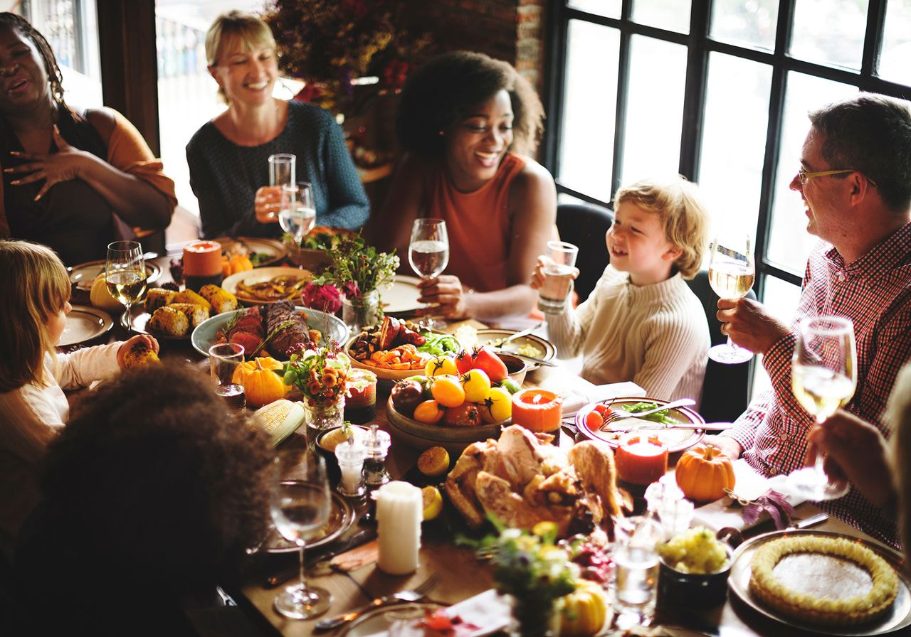 Group of family and friends laughing and raising glasses at a Thanksgiving dinner table.