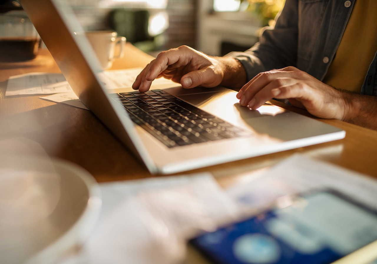 Hands typing on a laptop keyboard in a cozy workspace, with documents and a smartphone nearby.