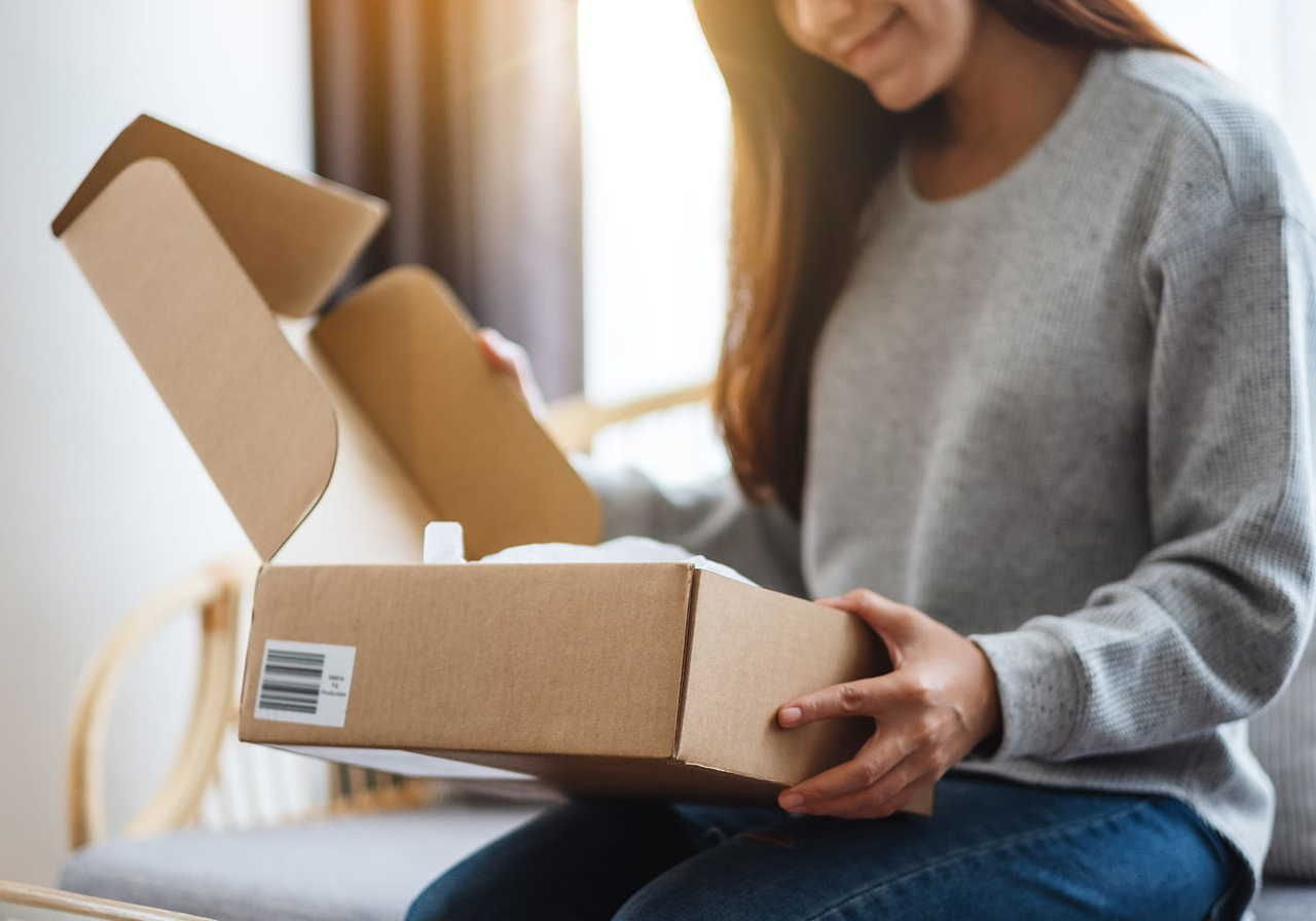 A woman opening a brown cardboard box while sitting on a chair.