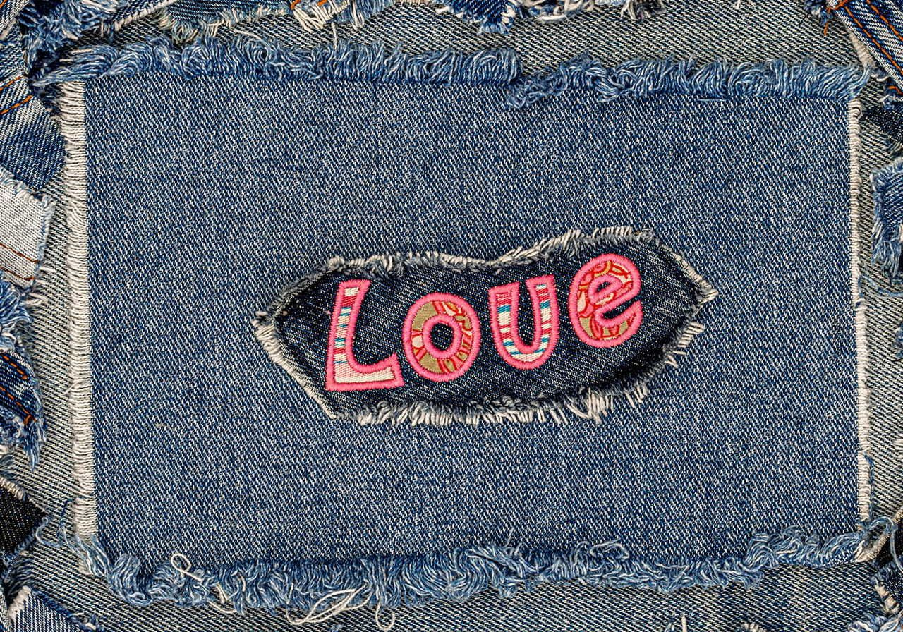 Close-up of a denim patch with frayed edges, featuring the word "Love" in colorful, embroidered letters.