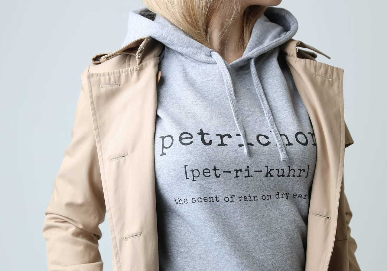 A person wearing a light grey hoodie with the word "petrichor" printed on it, along with a beige coat.