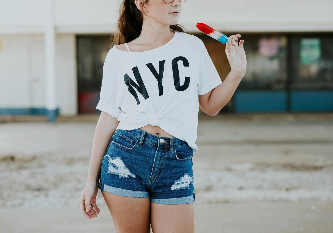A young woman in a white “NYC” t-shirt is eating ice cream.