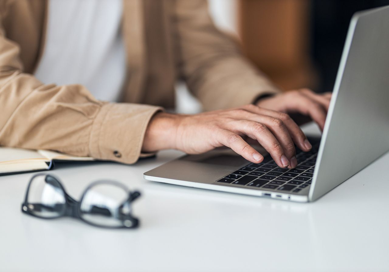 A person focused on typing on a laptop, with hands positioned on the keyboard and a screen displaying text.