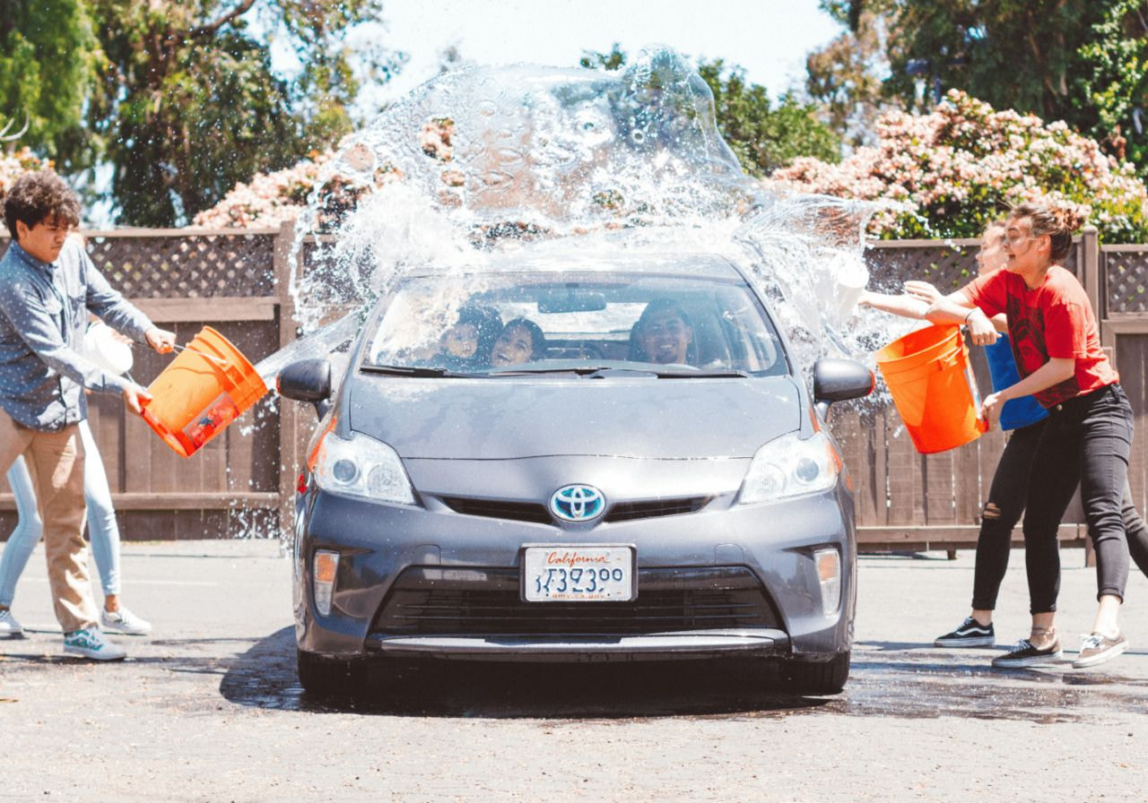 A few people are washing a car with soap and water, focused on cleaning the vehicle's surface in a residential area.