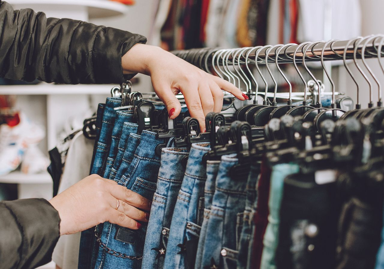 A woman examines a selection of jeans hanging on a rack in a clothing store.