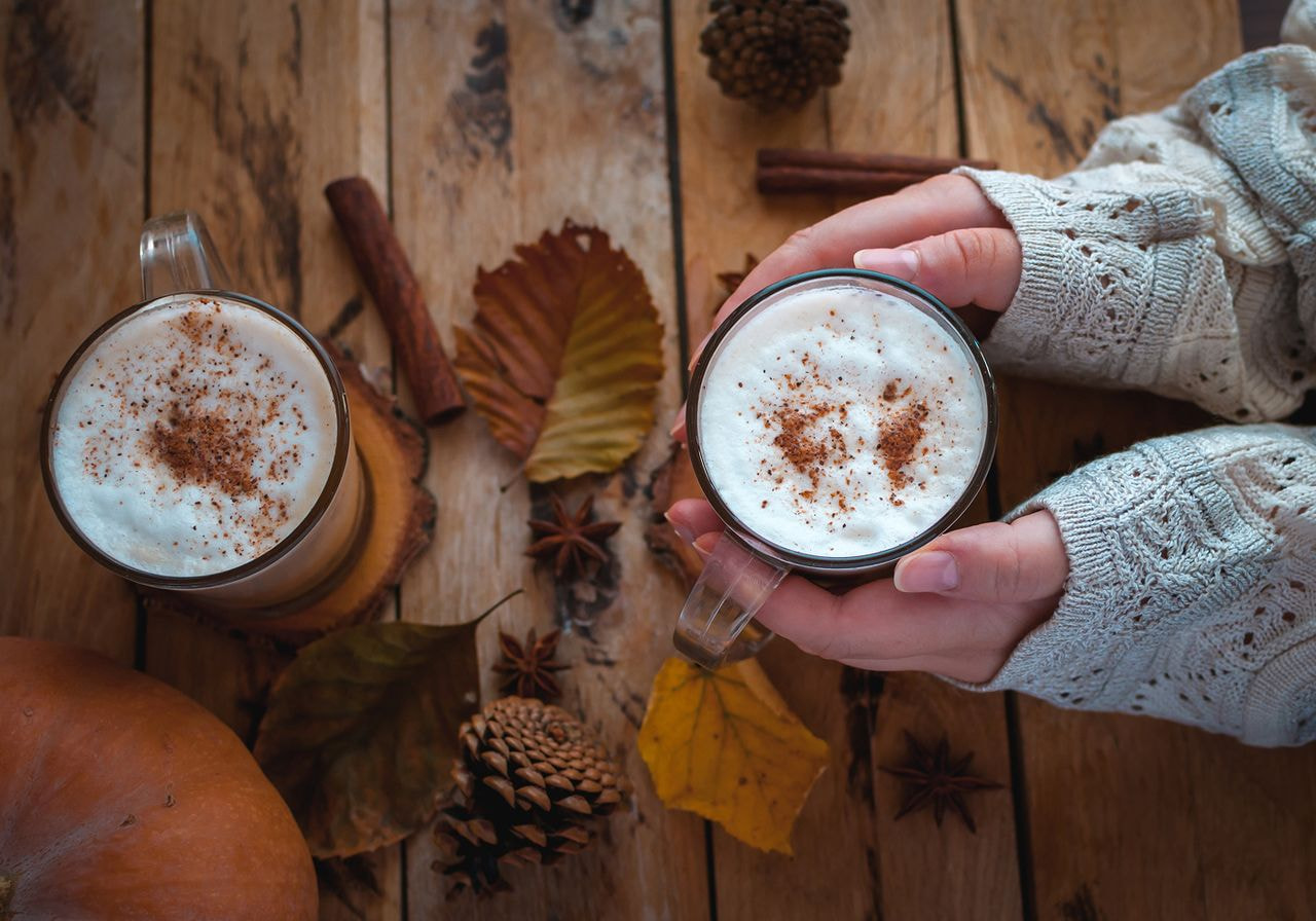 Two cups of coffee topped with cinnamon and pumpkin sit on a rustic wooden table.