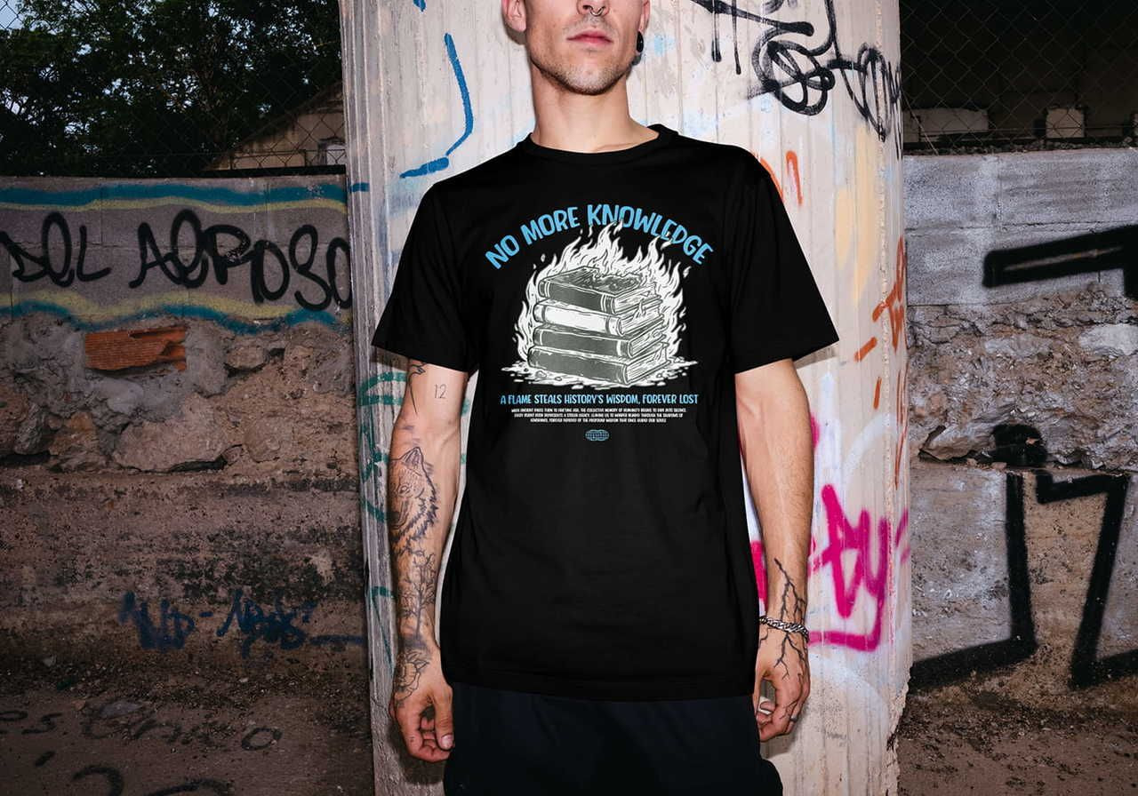 A man in a black t-shirt stands against a graffiti-covered wall. The shirt features flaming books and text "No More Knowledge”.