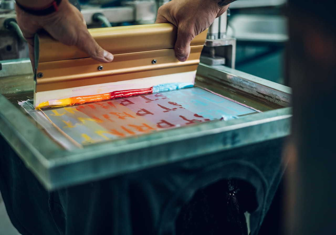 A person using a squeegee to apply colorful ink onto a screen printing frame.