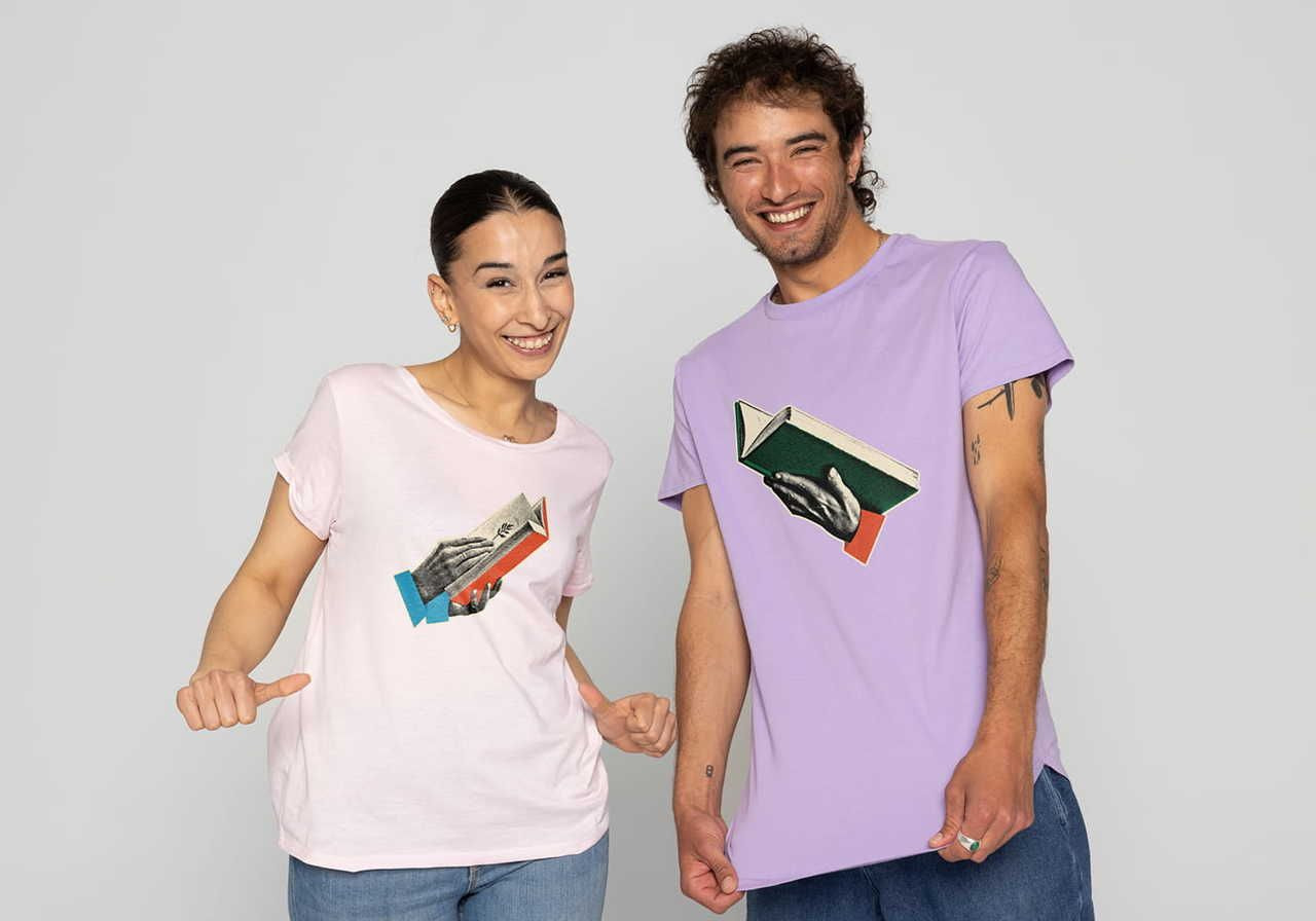 Two people stand side by side wearing graphic t-shirts; one in pink with a book graphic and the other in lavender with a different book graphic.