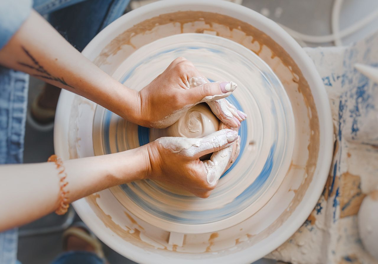 Hands shaping clay on a pottery wheel, with wet, earthy tones conveying creativity and focus.