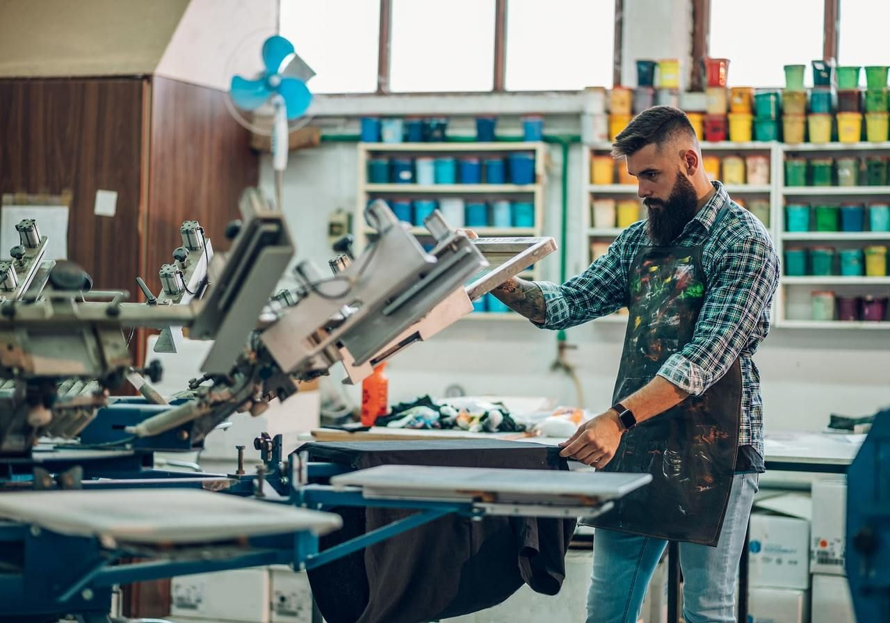 A man in an apron operates a machine, focused on his work in a workshop setting.