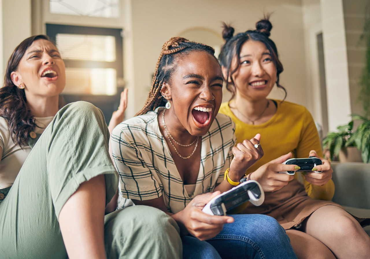 Three women are sitting closely together, laughing and enjoying themselves while playing video games.