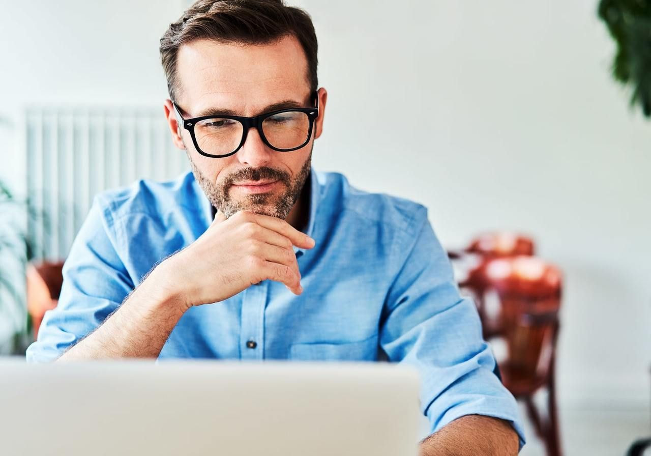 A man in glasses is reading from a laptop.