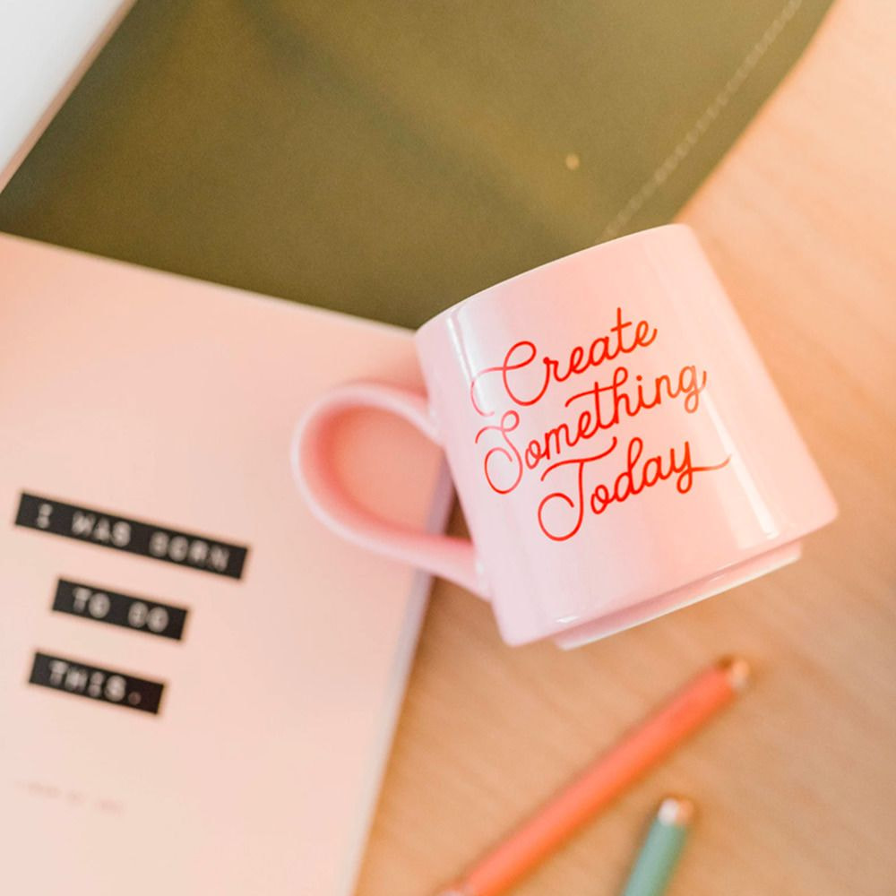 a pink mug with writing on it next to a notebook and pens