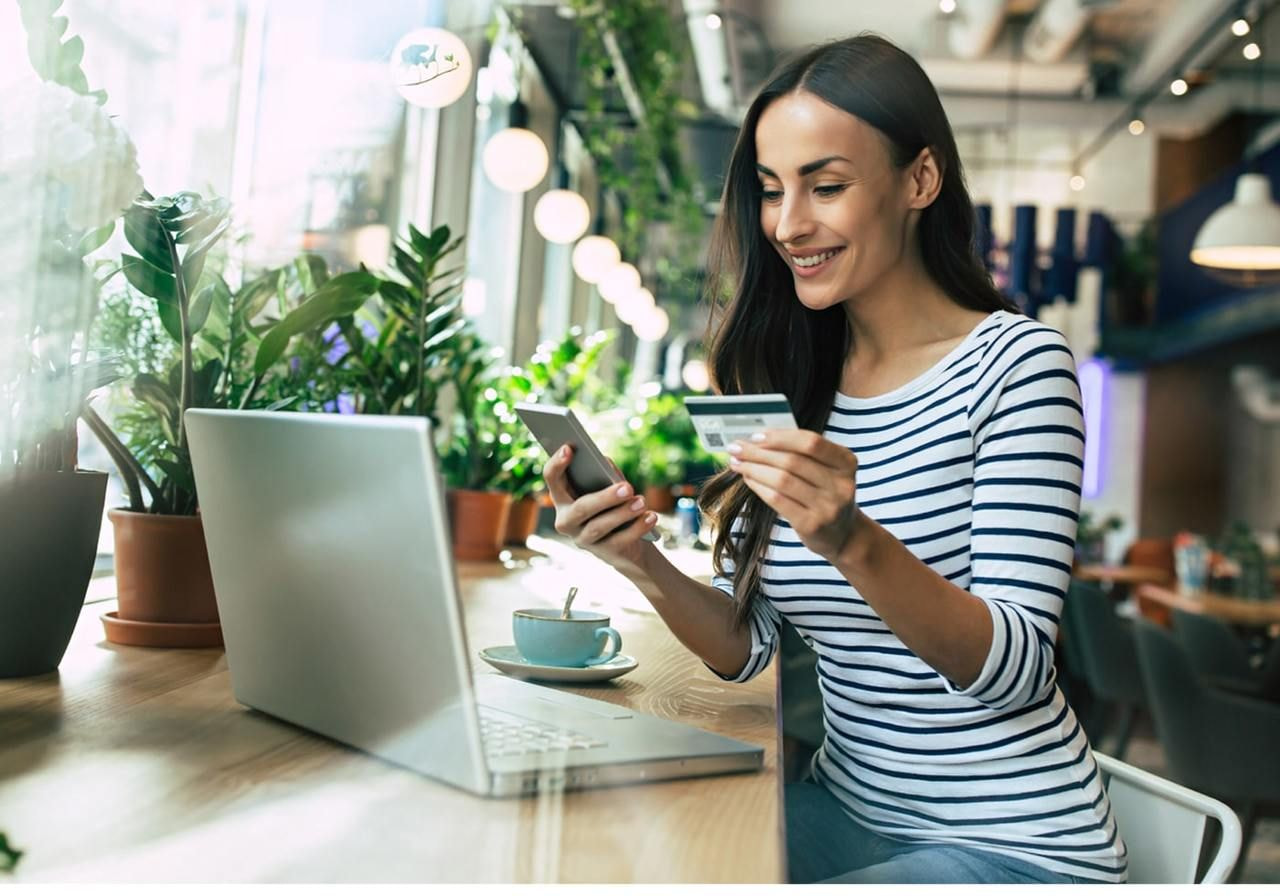 A woman sitting at a table, using her laptop and credit card to pay for her coffee.