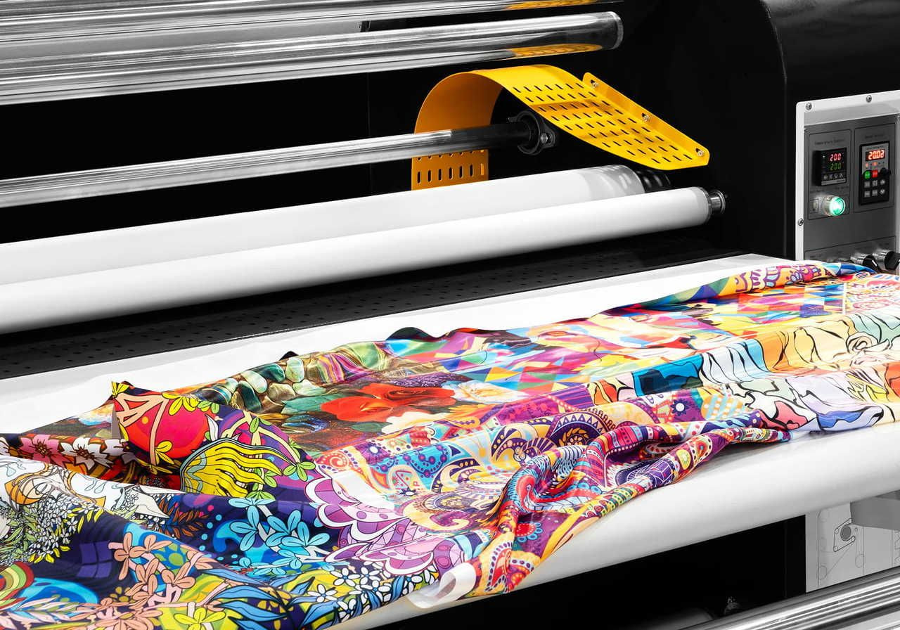 A vibrant, multicolored fabric with floral and abstract patterns is being printed by a sublimation printer. The machinery and control panel are visible.