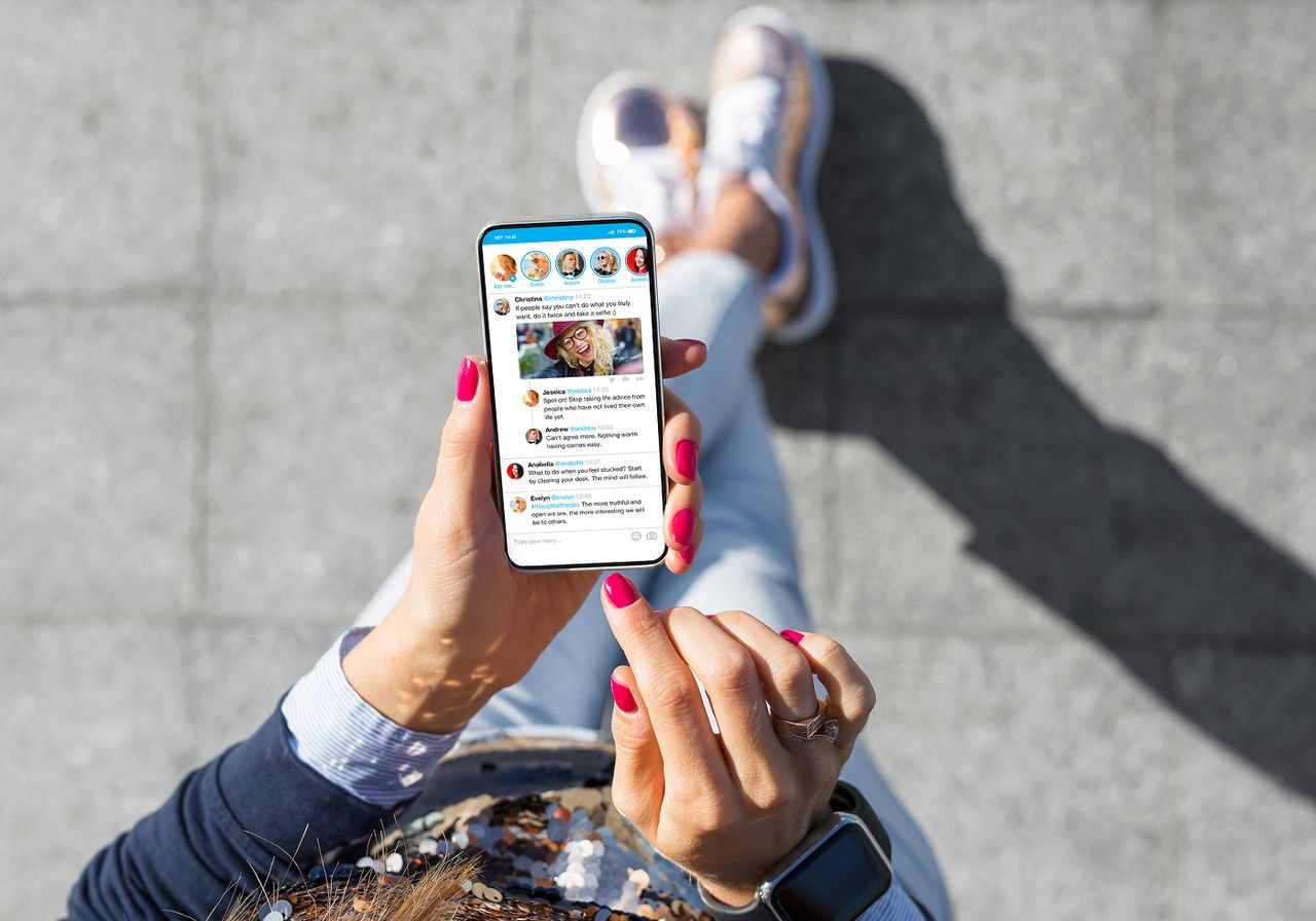 A person scrolls a social media feed on a smartphone while sitting outdoors, seen from above.