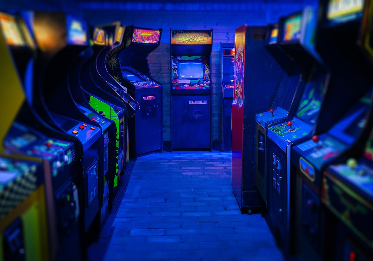 Dimly lit arcade filled with retro gaming machines, glowing in blue and neon hues.