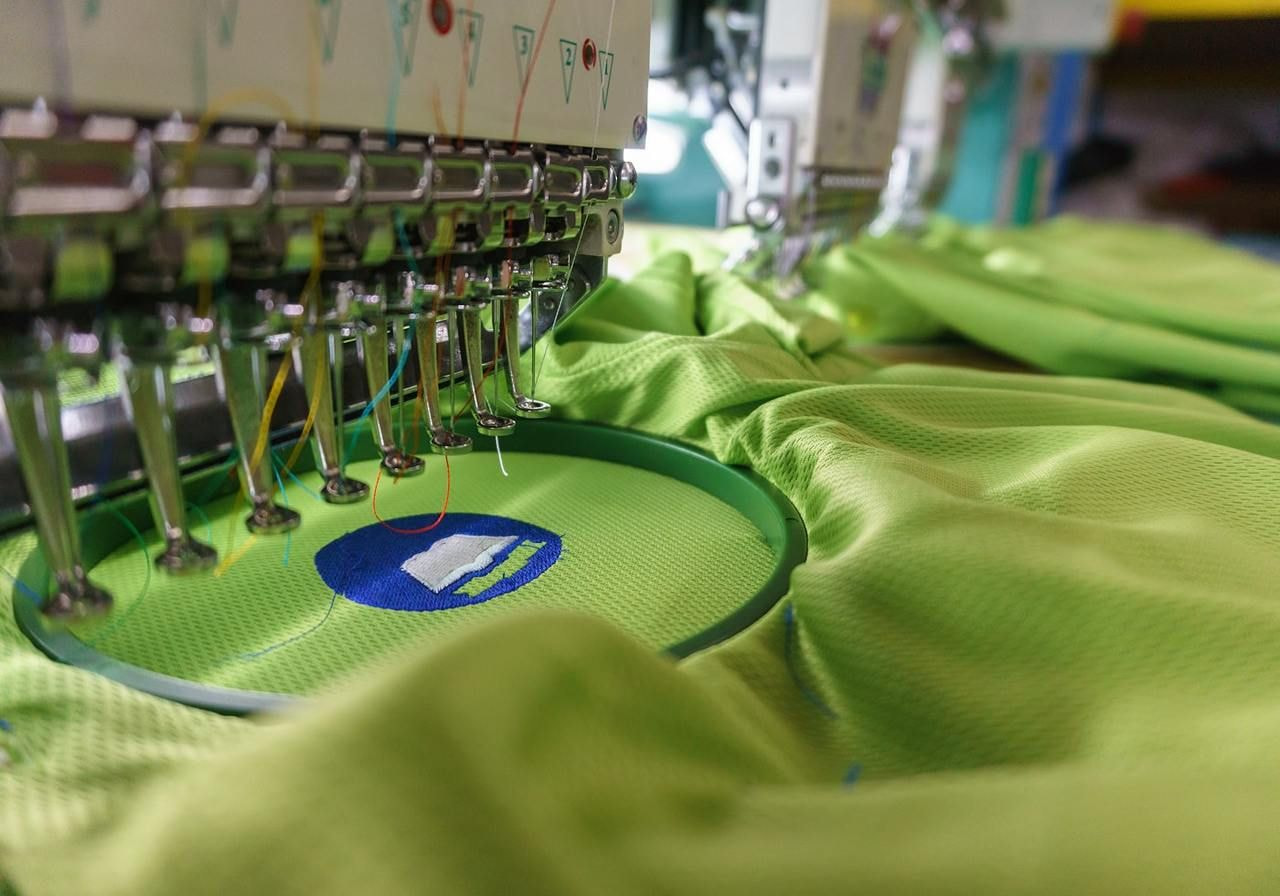A sewing machine stitching a green shirt, showcasing the fabric and the sewing process in action.