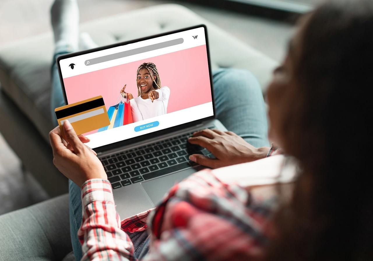 A woman is sitting on a couch in front of a laptop, holding a credit card to make an online purchase.