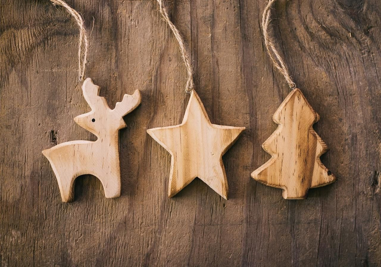 Wooden Christmas decorations hang against a rustic wooden background, creating a festive and cozy atmosphere.