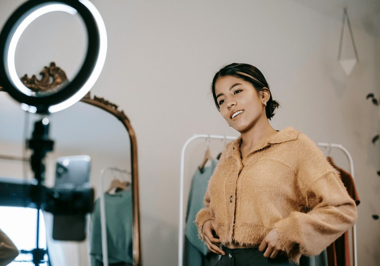A woman stands in front of a mirror, holding a camera and capturing her reflection.
