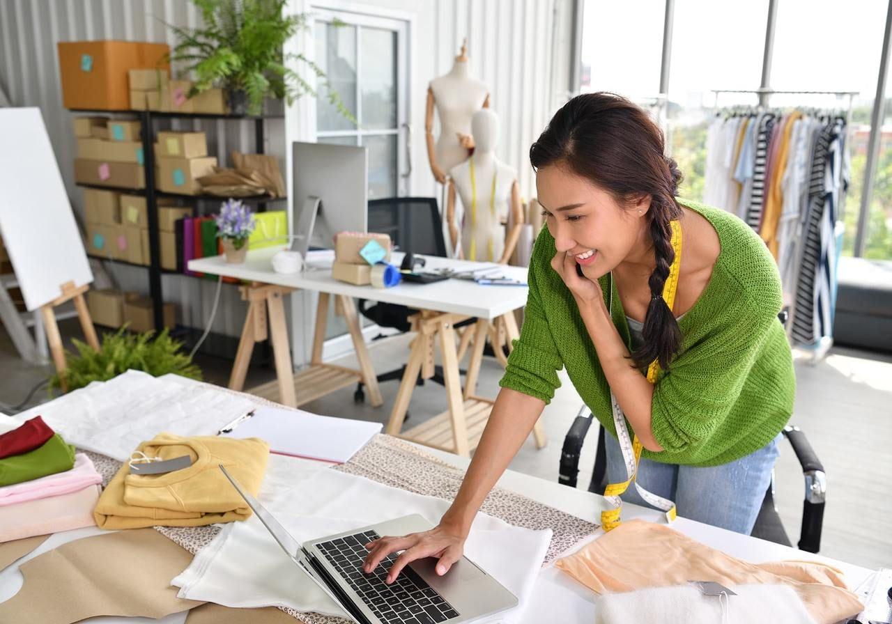 A woman is working on a laptop, talking on a phone.