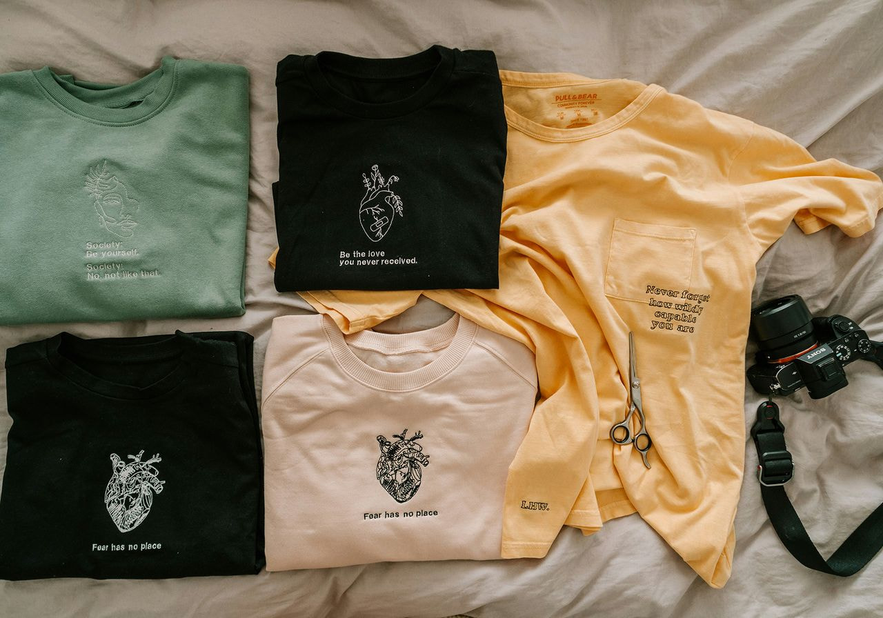 A young man and woman wearing colorful retro windbreakers, sunglasses, and headphones strike playful dance poses against a corrugated metal wall.