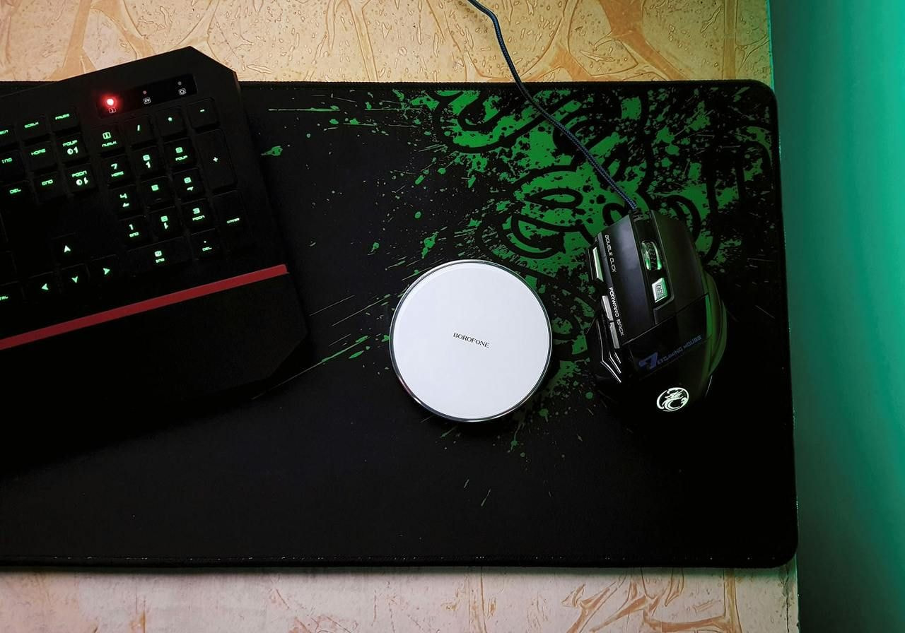 A computer mouse and keyboard on a desk, illuminated by a soft green light.